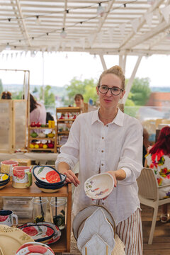 Woman Selling Handmade Leaf-Shaped Ceramic Plates with Floral and Fruit Ornaments at Summer Outdoor Craft Market
