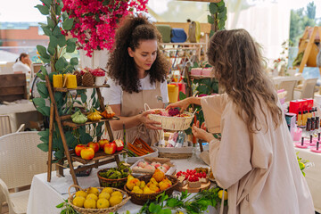 Woman Buyer Choosing Artistic Vegetable and Dessert Shaped Candles on Display Table at Summer Artisan Market