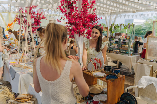 Female Artisan at Outdoor Summer Fair Displaying Handcrafted Ceramic Plates with Botanical and Fruit Patterns