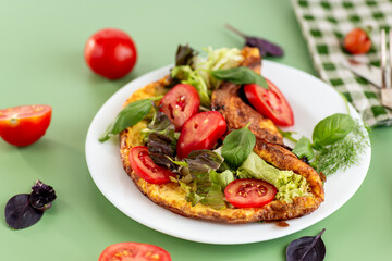 Delicious omelette on a plate with fresh leaves and tomato slices