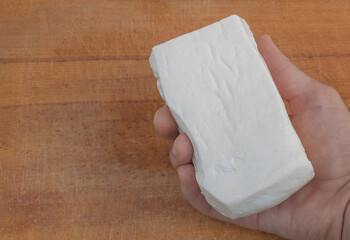 Traditional white cheese block held in hand on rustic wooden table