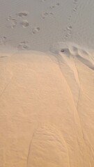 Minimalist top down view of human footprints on a rippled sand dune. Natural abstract background concept of travel, journey, and exploration in a vast, empty desert landscape.