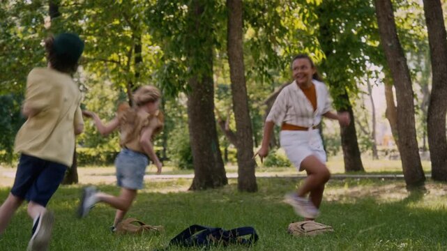 Multiethnic group of energetic children running around in park playing tag while having fun after school classes on green lawn celebrating beginning of summer vacation