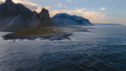 Orange Lighthouse on Volcanic Coastline with Mountain Backdrop in Iceland