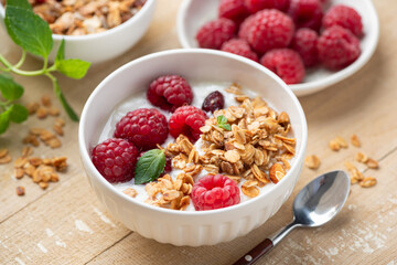 Yogurt bowl with crunchy granola and raspberries topping on wooden table background
