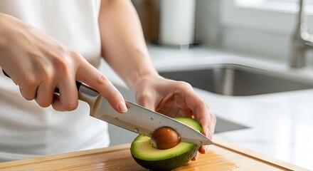 Obraz premium Close-up of a person's hands slicing a ripe avocado in a kitchen setting.