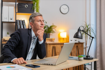 Young businessman entrepreneur prepares startup project for presentation finds idea. Employee freelancer thinking while sitting with laptop computer at home office desk. Remote distant working.