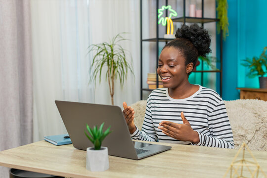 African American young girl participating in video conference at home. Gesturing actively, showing presentation on laptop. Confident expression, sitting on sofa, engaging online communication indoors