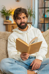 Indian man reading interesting book, turning pages smiling enjoying literature, taking a rest on...