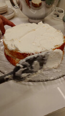 Close-up of a pastry chef's hands spreading white cream frosting on a delicious homemade layer cake with a spatula. The process of decorating a dessert for a special occasion or birthday party.