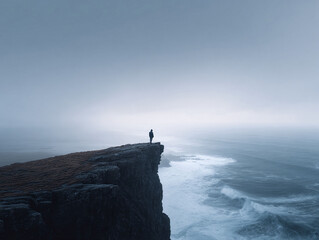 Moody seascape featuring a lone figure standing on a dramatic cliff edge overlooking crashing waves. Evokes themes of solitude, contemplation, and the power of nature.