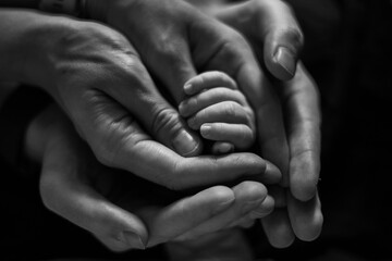 The hand of a newborn baby, tenderly held by the hands of mother and father as a support for a new life in black and white color