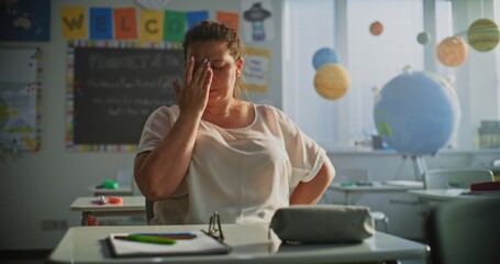 Tired Female Teacher Sitting Alone in Empty Classroom, Relaxing After Class. Woman Feeling Stress, Burnout and Mental Exhaustion in Educational Environment, Working in Elementary School. Slow Motion.