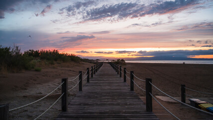 Obraz premium Wooden boardwalk leading to the sea at sunset with colorful clouds