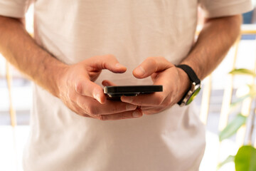 Close-up of man in white t-shirt typing message on mobile phone