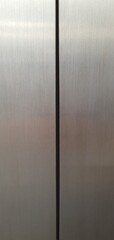 Close-up of stainless steel elevator doors with vertical seam. Minimalist industrial background with brushed metal texture, clean lines, and modern design
