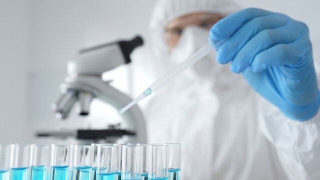 Scientific researcher wearing protective equipment, carefully pipetting liquid into test tubes while conducting medical research experiment. Medicine, healthcare and science concept