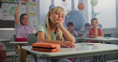Fototapeta premium Sad Primary School Girl Sitting at Desk, Getting Tired During Lesson or Upset Because of Bad Grade on Homework. Group of Young Children Learning Science or Geography in Modern Classroom. Dolly Shot.