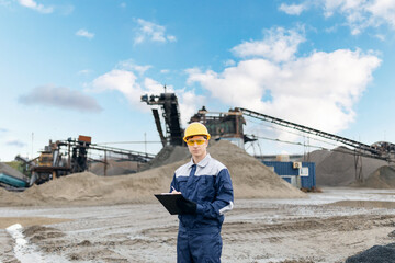 Portrait worker surveying engineer in sand quarry with mining equipment