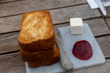 Three slices of toasted bread on a wooden board with a piece of butter and jam.
