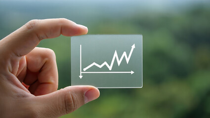 Hand Holding a Transparent Square with an Upward Trending Graph A Visual Representation of Business Growth and Financial Success Against a Blurred Green Backdrop