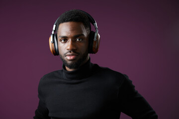 Stylish young Black man in a black turtleneck wearing headphones against a purple background, expressing focus and confidence in a modern setting