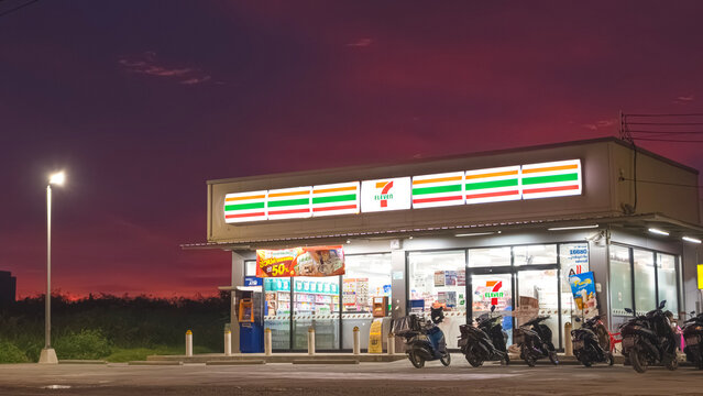 Samut Sakhon, Thailand - August 03, 2025 : 7 Eleven convenience store with illuminated logo sign lighting and row of motorcycles parked in parking lot service area against twilight sky background