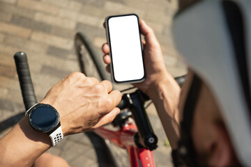 Male cyclist in helmet with mobile phone with white blank screen on bike check apps at park. Space for design. View from above. Close up.