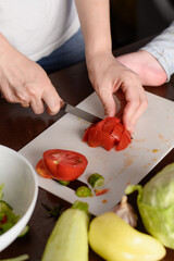 Woman carefully cutting fresh tomato on cutting board preparing to cook food in kitchen, fresh salad,close-up. Cooking concept