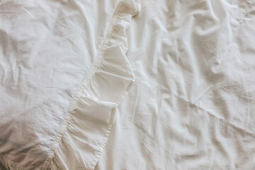 Soft white fabric with ruffled edge displayed on a bed during daylight hours