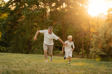 Fototapeta premium Father and son playing and running together outdoors during a sunny evening