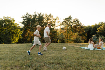 A family spends time outdoors playing soccer and relaxing on a picnic blanket.