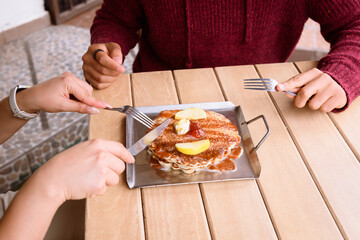 Unrecognizable Couple sharing and feeding each other some Hot cakes or pancakes with maple syrup, butter, and fruit