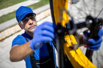 Bike mechanic repairs bicycle in outdoor workshop, focusing on wheel adjustments during bright sunny day