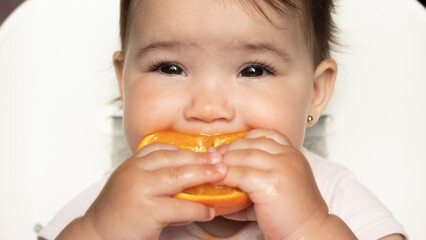 Baby eating half an orange, healthy snack and nutrition concept