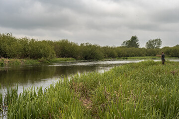 Man Fishing by a Calm River Surrounded by Lush Greenery in Belarus