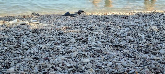 Close-up of pebbles on beach with sandals and sea waves in background
