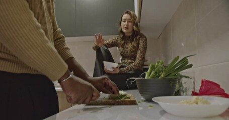 A young couple is cooking together in their modern kitchen. They are chopping vegetables and having a conversation. - Powered by Adobe