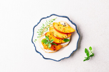 Fresh juice toast with peach slices, cream cheese, sesame seeds and aromatic herbs on light stone table top view.