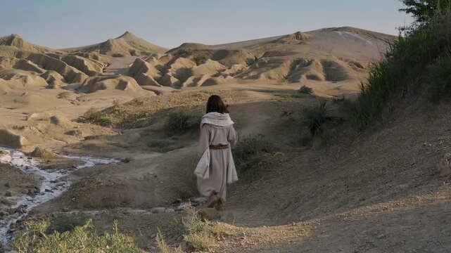 A mysterious man in a white robe following the path through the sandy mountains of the Judean wilderness. Large crane shot