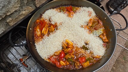 Traditional paella preparation with rice and seafood on grill - spanish cuisine experience. Rice in the shape of a cross in paella. Stage of cooking paella. Ingredients for paella