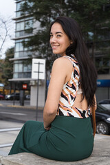 Young latin woman smiling and relaxing on a bench in the city