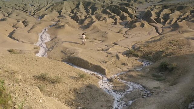 Mysterious silhouette walking through the sandy hills of the Judean desert, drone camera reveals the distant green landscape from above. Tilt down crane movement