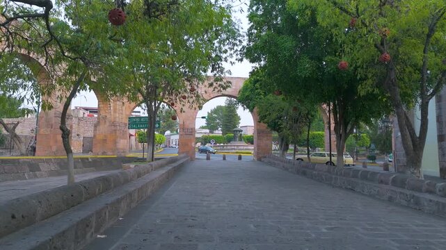 Morelia, Mexico: a calm morning in the capital at the Las Tarascas fountain. The old aqueduct frames the city scene where pedestrians and vehicles begin to bring life to the city.