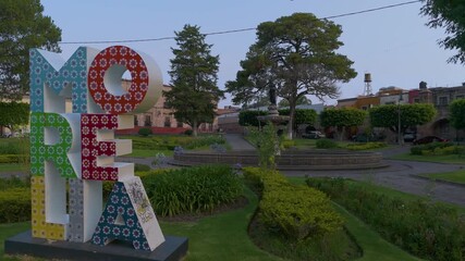 Morelia, Mexico: A colorful sign bearing the name of the capital, Morelia, adorns the Villalongín public garden, which features a central fountain.