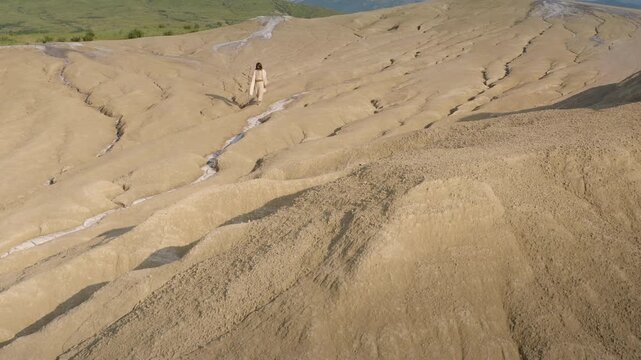 Mysterious man walking down a sandy hill wearing a white robe holding a wooden staff. Aerial backwards out shot