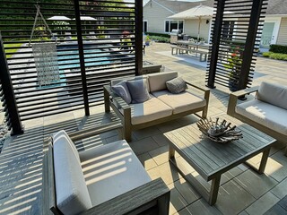 Modern indoor outdoor living entertainment space and patio under a pavilion pergola. poolside equipped with bar and gas fire pit with cascading waterfall. Chair sofa couch and table. Hotel resort feel