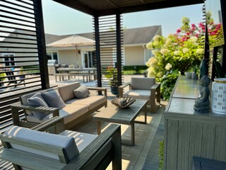 Modern indoor outdoor living entertainment space and patio under a pavilion pergola. poolside equipped with bar and gas fire pit with cascading waterfall. Chair sofa couch and table. Hotel resort feel