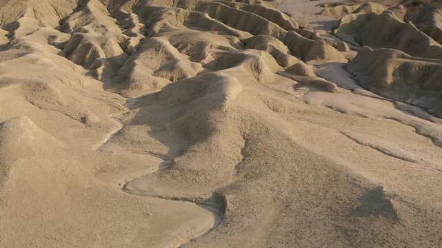 A lone man with long hair, dressed in a robe, walking down a sandy hill from a mountain. Aerial establishing shot