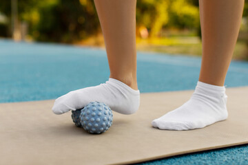 Woman's leg doing massage with an orthopedic spiny plastic massager, standing on fitness mat, closeup. Self myofascial release concept